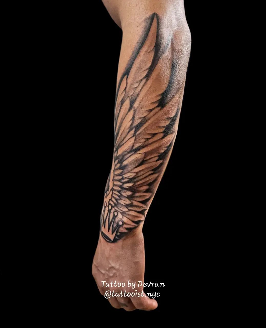 A large black and gray feathered angel wing tattoo extending along the forearm.